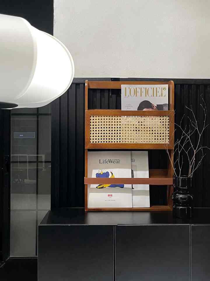 Black and wood-tone living room corner featuring a magazine rack centrally placed in a simple setting