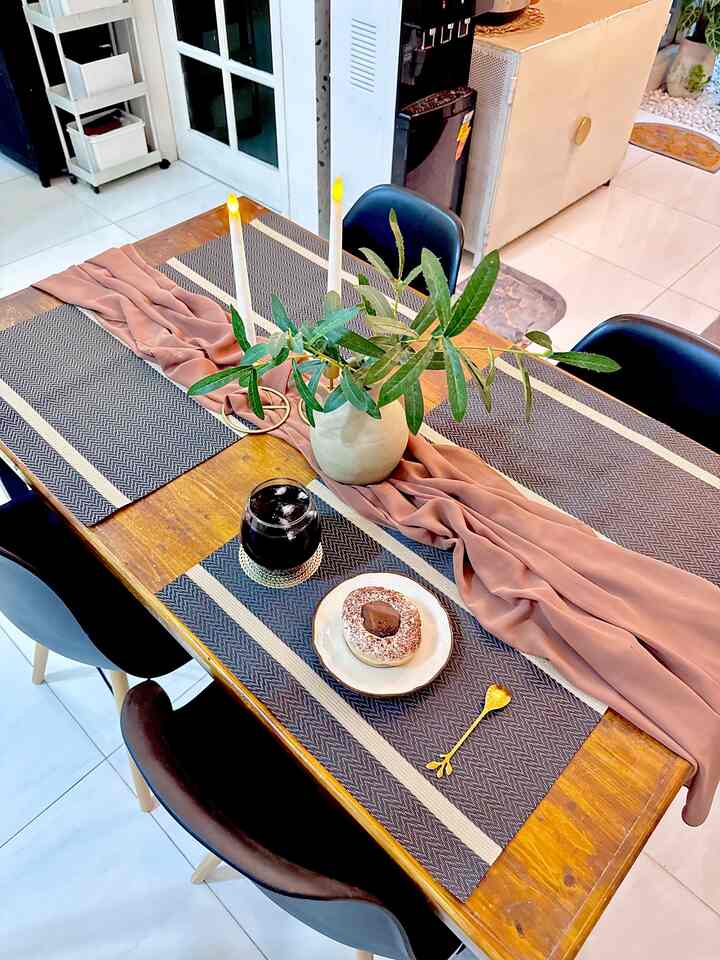 Wood tone dining table with black chairs in living room dining space, featuring a vase with greenery and candles creating a cozy atmosphere