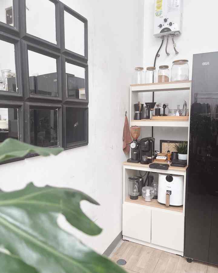 Modern kitchen corner in white and black tones featuring coffee equipment on storage shelves and large black-framed mirrors, creating a clean atmosphere