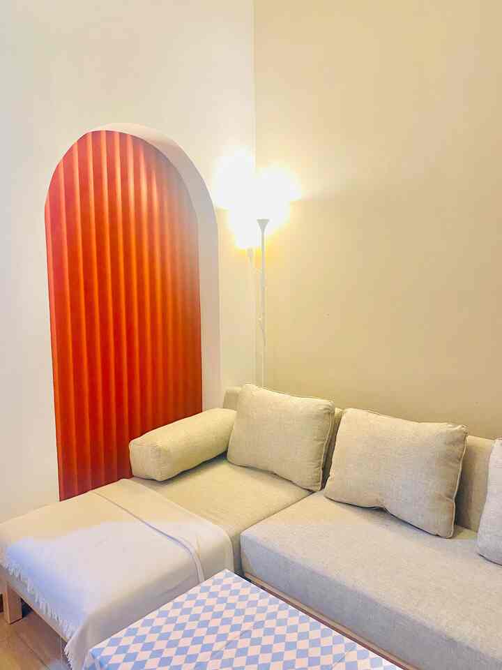 Beige-toned living room featuring a beige sofa and orange curtain in an arched niche, creating a cozy atmosphere