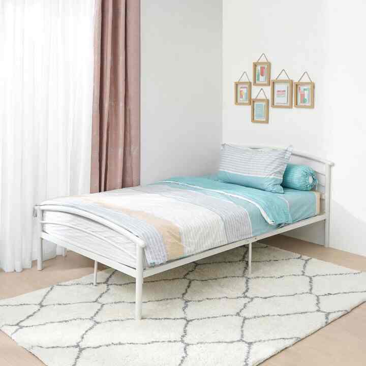 Modern bedroom with white walls and beige area rug, featuring a white metal bed with blue bedding