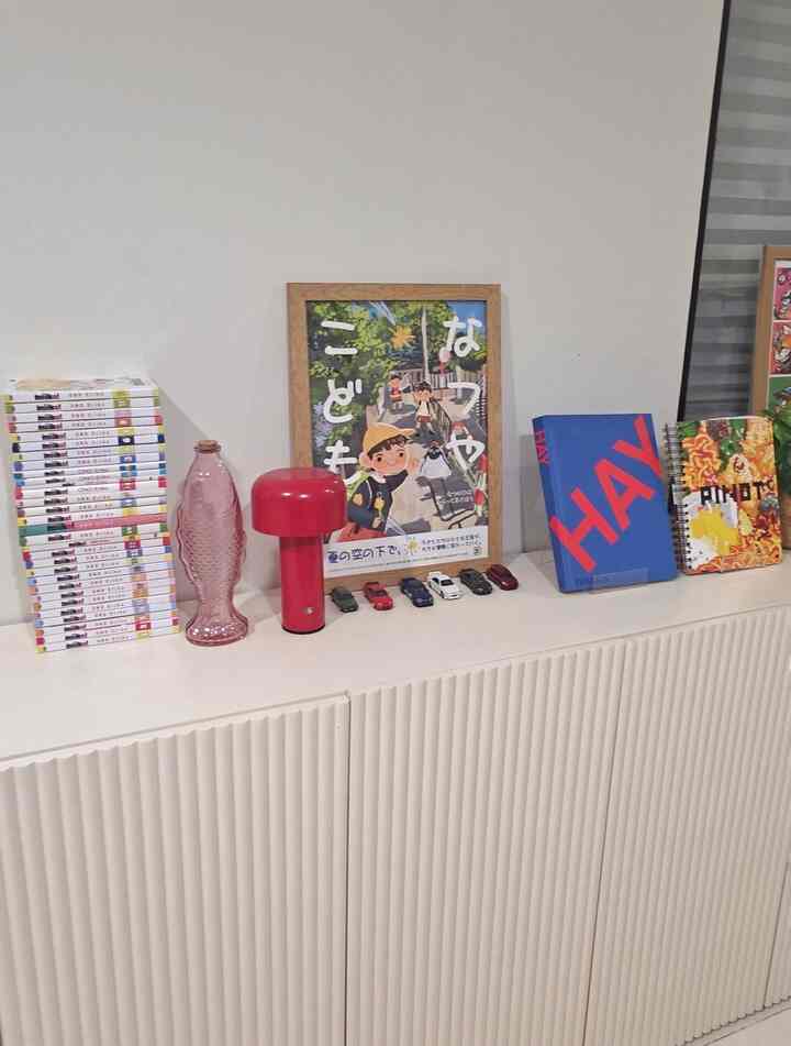 White-toned wall and cabinet topped with red table lamp, books, and framed picture in a cozy setting