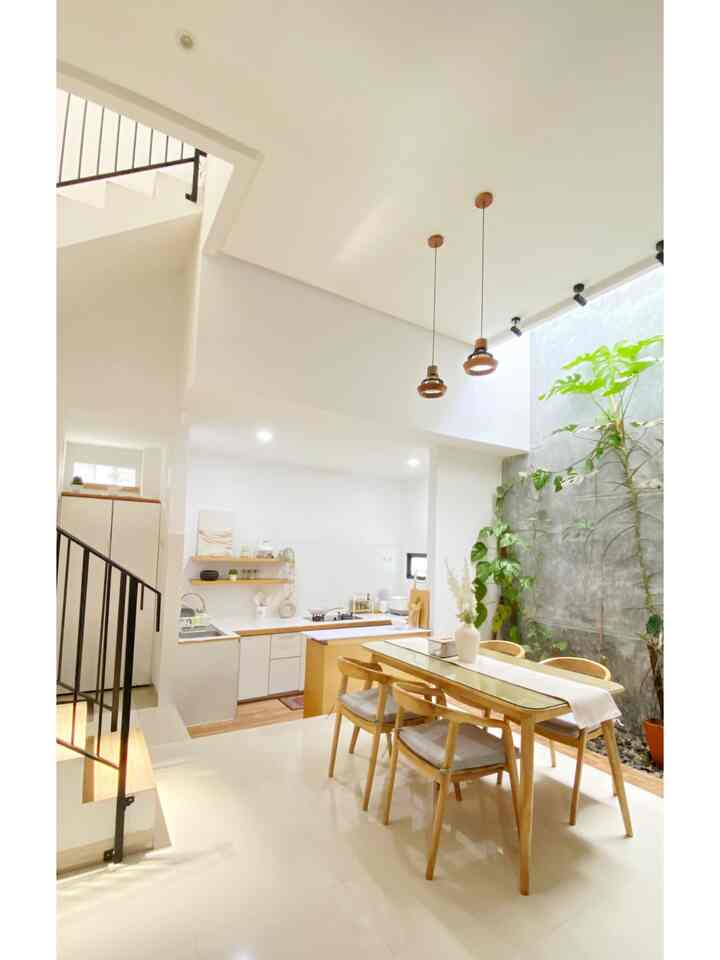 Open Space Kitchen & Dining Area – Rumah Aswira
Ruang ini mengusung konsep terbuka dan menyatu, di mana dapur dan ruang makan berada dalam satu area tanpa sekat permanen. Desain ini menciptakan kesan lapang, terang, dan hangat—ideal untuk hunian modern yang mengedepankan kebersamaan.

Detail Karakteristik:

Tata letak terbuka (open plan) memungkinkan aktivitas memasak dan bersantap berjalan berdampingan, memudahkan interaksi antar anggota keluarga atau tamu.
Dominasi warna putih dan elemen kayu alami menciptakan suasana minimalis yang bersih dan menenangkan.
Pencahayaan alami yang masuk dari atas (void) dan bukaan besar, memberi kesan segar dan terang sepanjang hari.
Tanaman monstera deliciosa indoor di sudut dinding beton ekspos menambahkan sentuhan tropis yang hidup, menciptakan harmoni antara alam dan desain interior.
Lampu gantung bergaya industrial-minimalis di atas meja makan memberikan sentuhan estetika sekaligus pencahayaan hangat saat malam.
Meja makan kayu dengan empat kursi menjadi pusat ruangan—simbol kehangatan dan tempat berkumpulnya cerita keluarga.
Dapur praktis dan compact dengan layout linier, menghadirkan efisiensi namun tetap estetis berkat open shelving dan aksen natural. #BTNOAS11 #RumahOpenSpace #RumahTanpaSekat