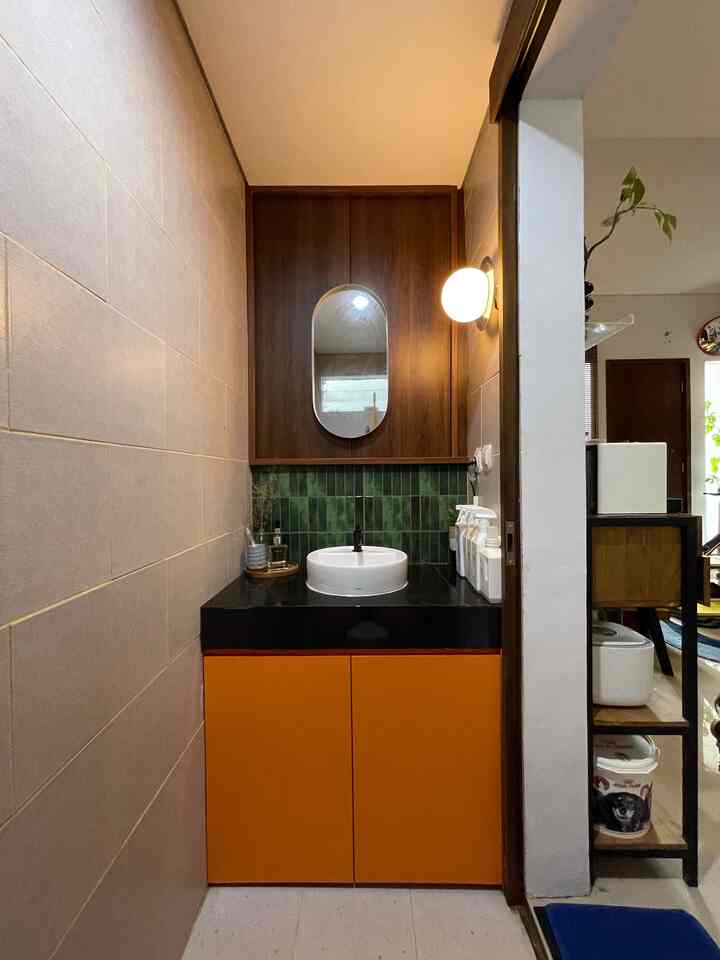 Cozy powder room with orange cabinets, brown wooden panels, and green tiles accentuating storage area
