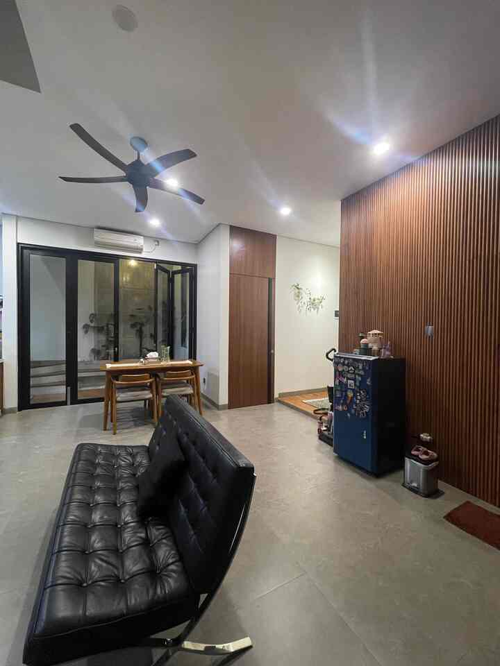Modern living room with white walls and ceiling, featuring a black sofa and wood-toned dining table in a tidy setting