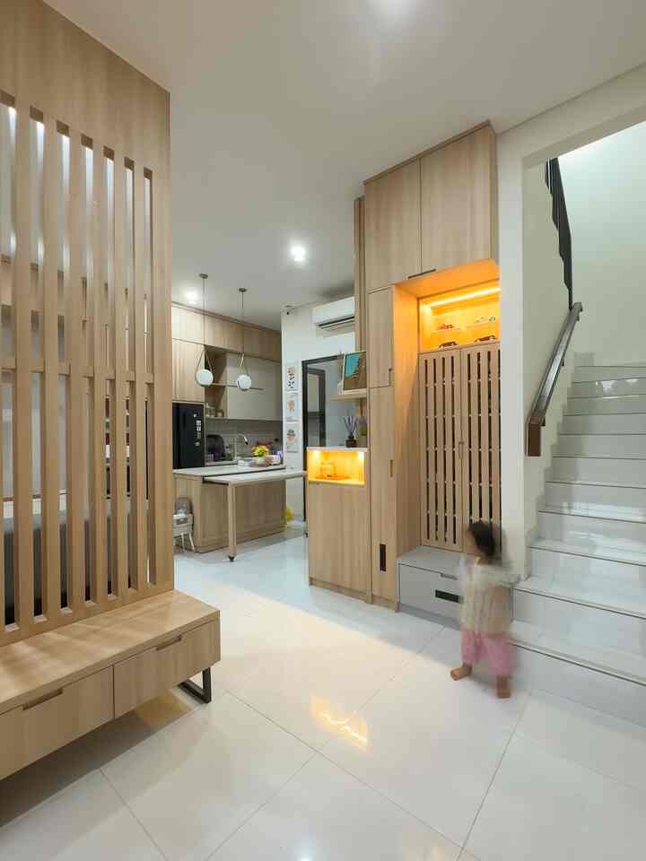 Natural wood tone minimalist entrance and hallway featuring slatted partition on left, storage cabinets near stairs, and shoe bench in a clean setting