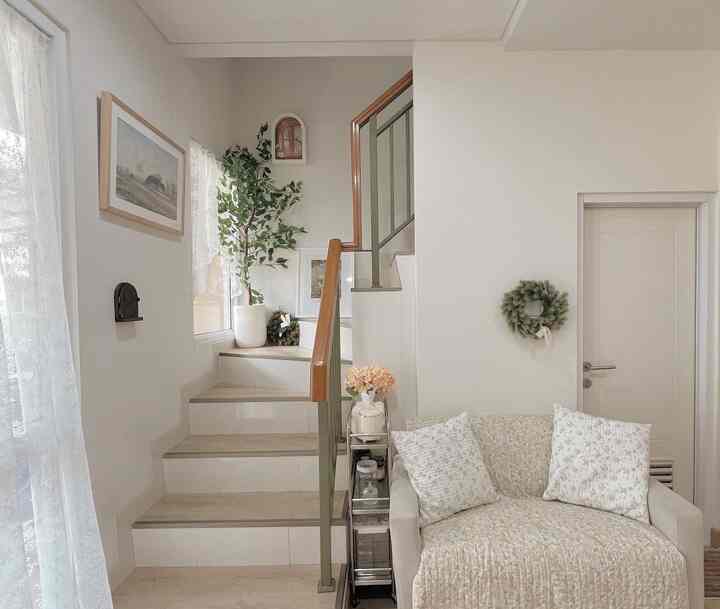 Natural beige-toned living room featuring a loveseat sofa and staircase with a clean, cozy atmosphere