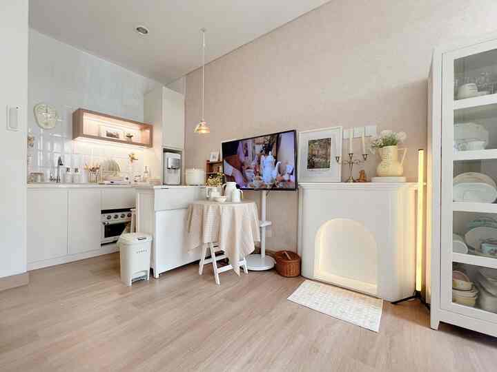 Ivory and white toned open living room and kitchen space with a small dining table and faux fireplace creating cozy minimal interior