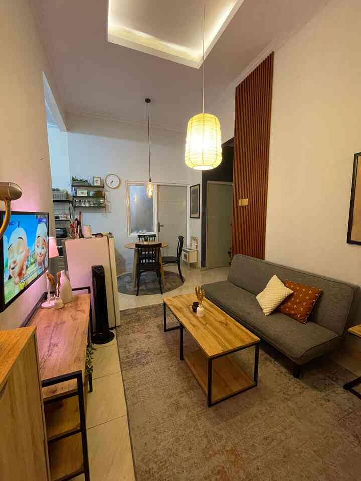 White-walled, wood-toned small apartment living room featuring a comfortable sofa bed, dining table, and warm lighting creating a cozy atmosphere