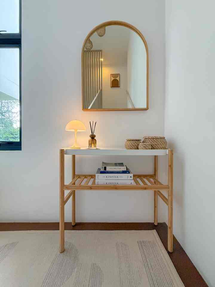 Bright white and wood tone entrance area featuring an arched mirror and simple table in a minimalistic design