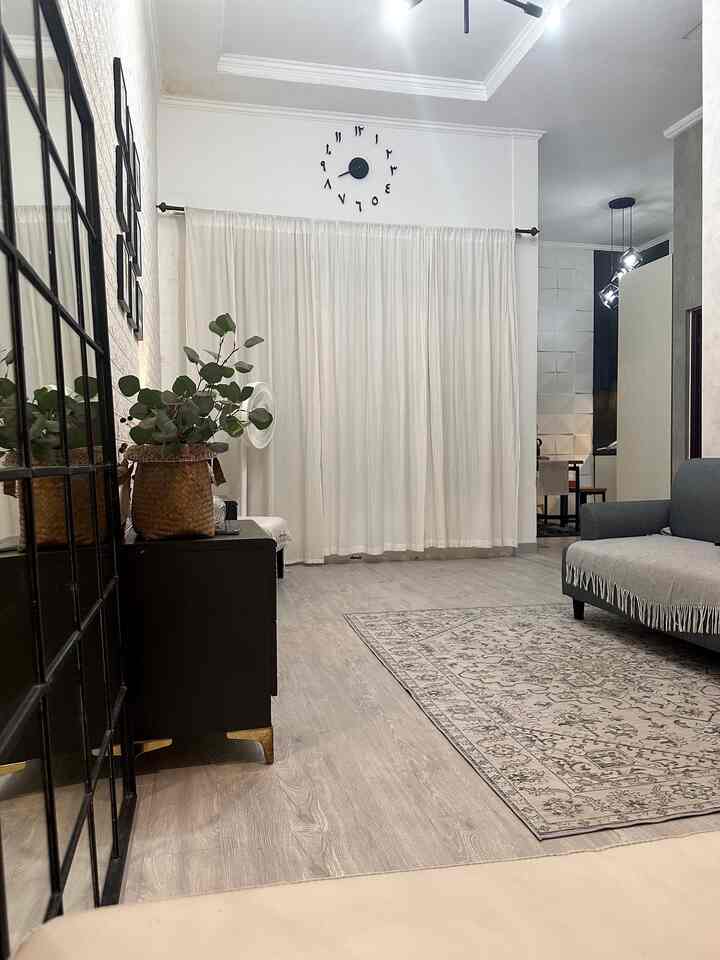 A white-toned living room featuring a gray sofa, carpet, and wood-tone flooring in a simple, harmonious space