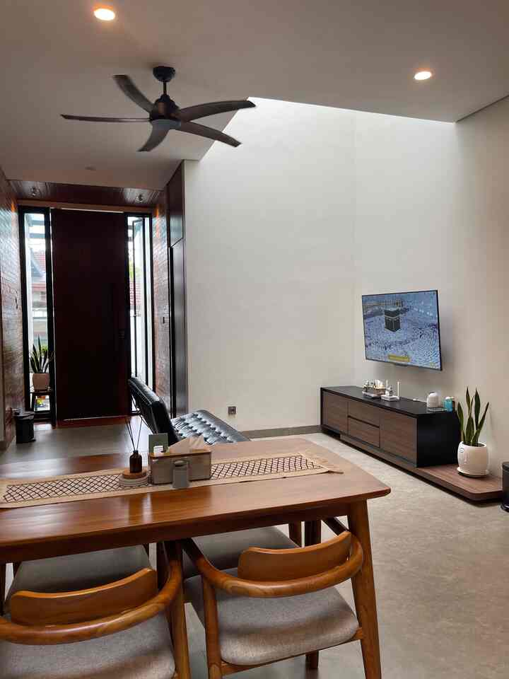 Wood-tone and modern styled living and dining room featuring black leather sofa and wall-mounted TV in a spacious, clean interior