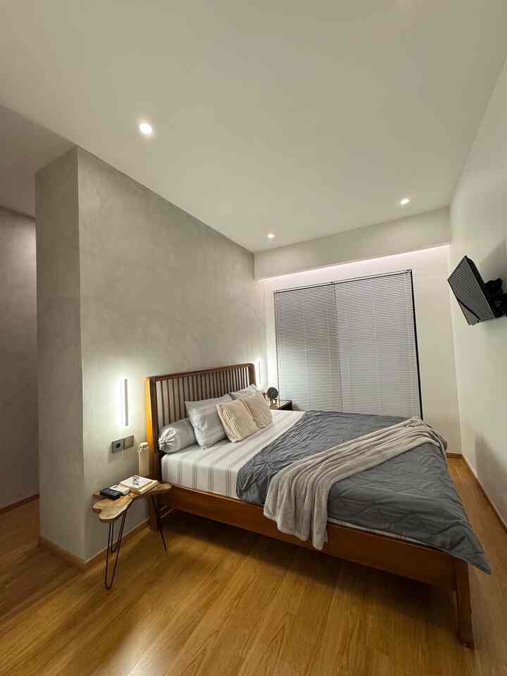 A neat bedroom featuring natural wood tones and gray bedding, accented by lighting and a nightstand