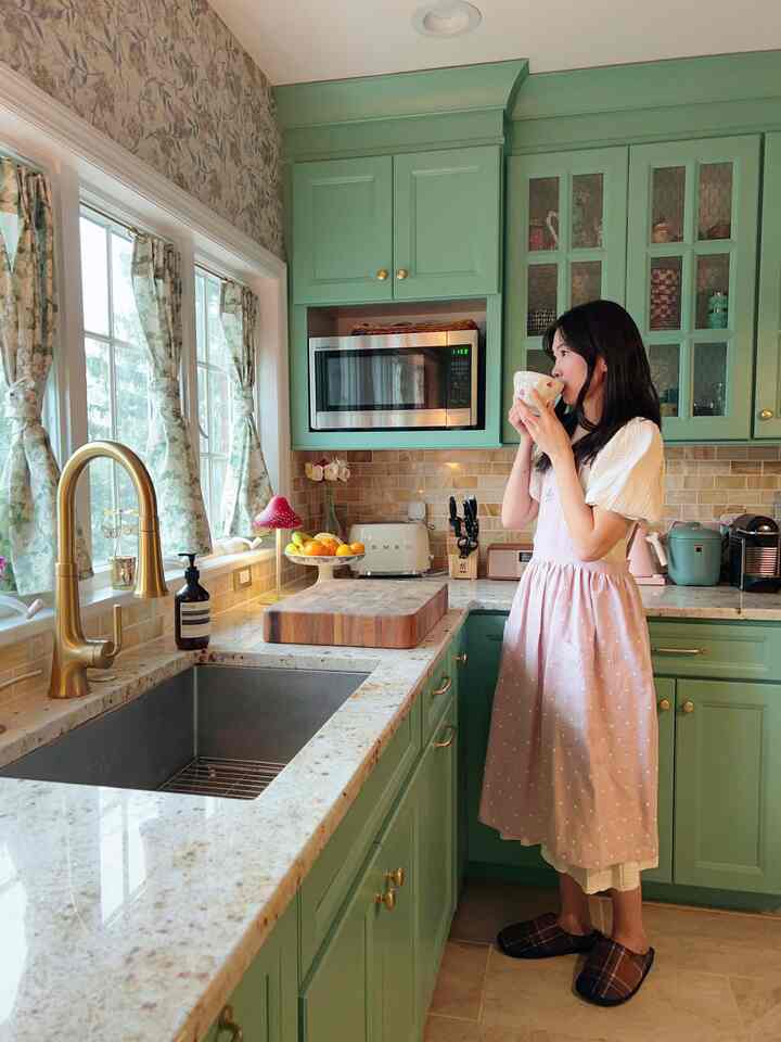Khaki-toned kitchen featuring a woman in a pink apron sipping from a cup, creating a cozy, cottagecore-inspired atmosphere
