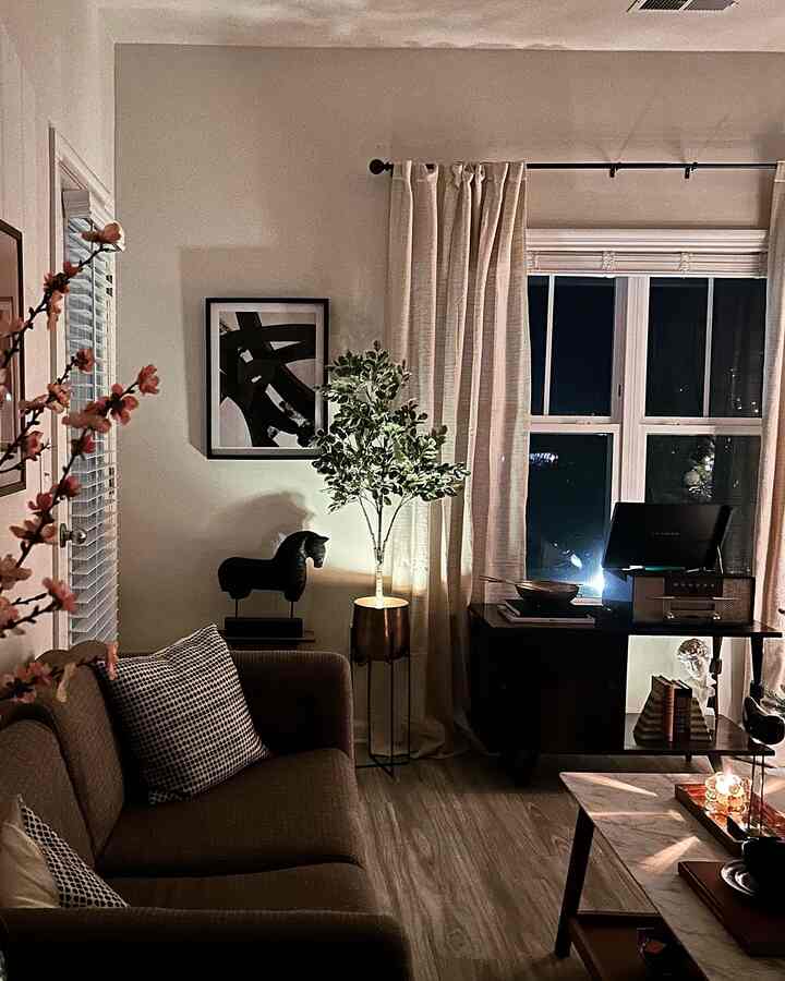 Natural modern living room at night featuring a brown sofa, beige curtains, and a green plant with ambient lighting