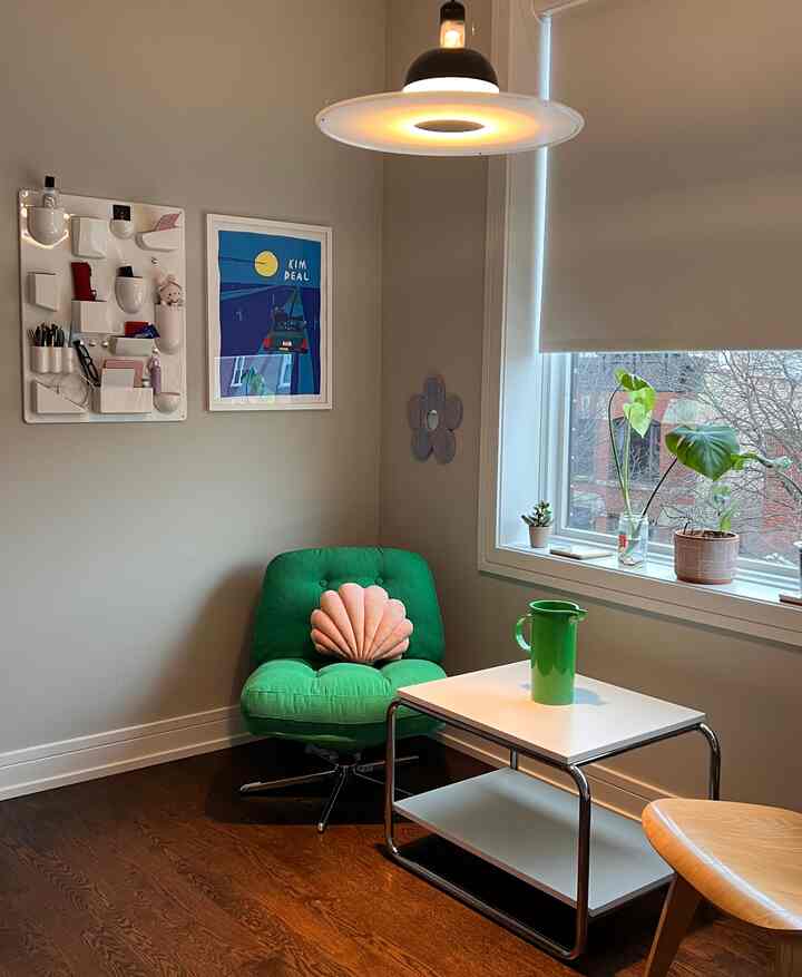 Cozy home office corner with gray walls and wooden floor featuring a green armchair, white side table, and a pendant light overhead