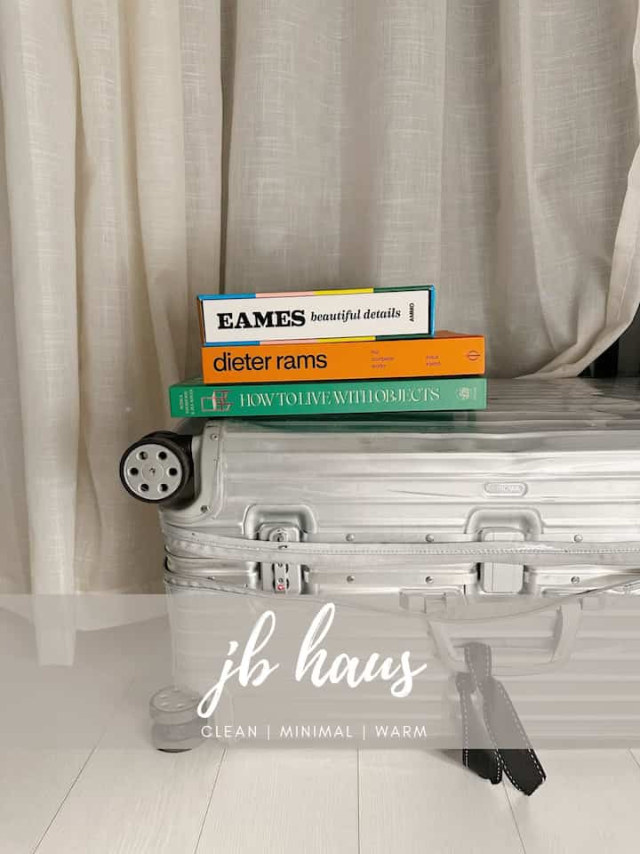 Minimal space featuring a silver suitcase stacked with three design books against beige curtains background