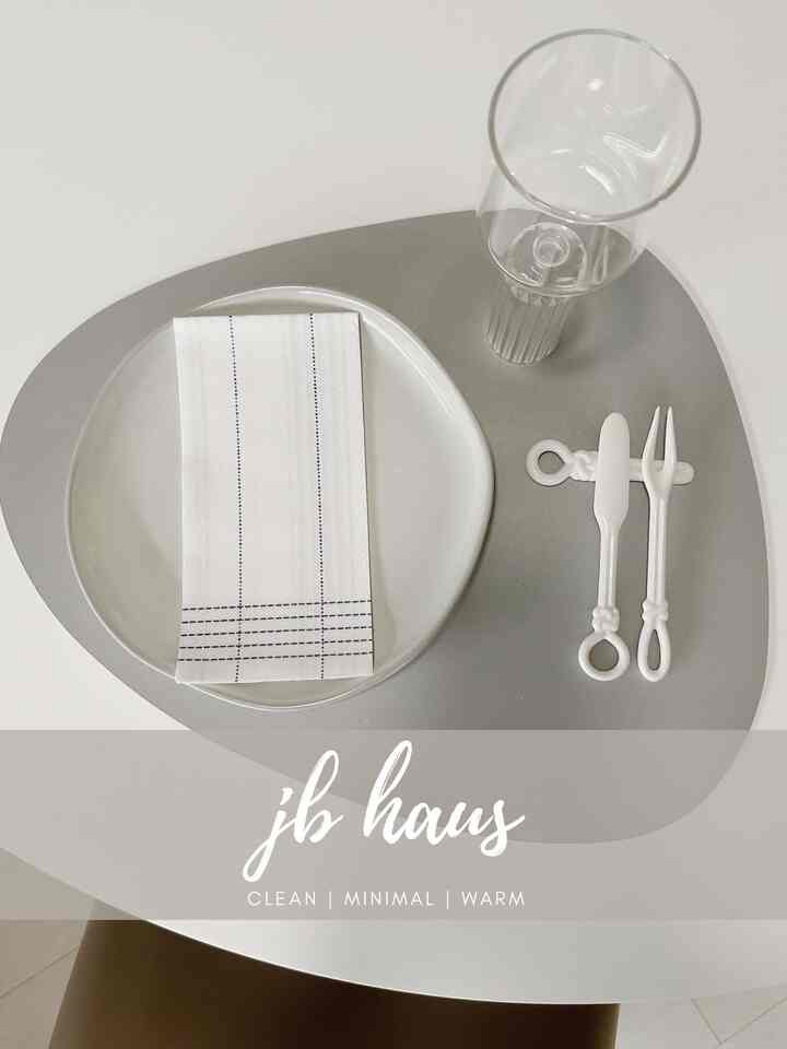Simple dining room in white and light gray tones featuring a minimal table setting with plate, glass, and cutlery