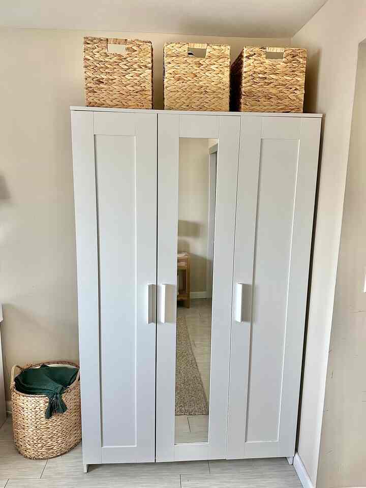 White-toned wardrobe with natural wicker storage baskets on top, creating a simple and organized storage space