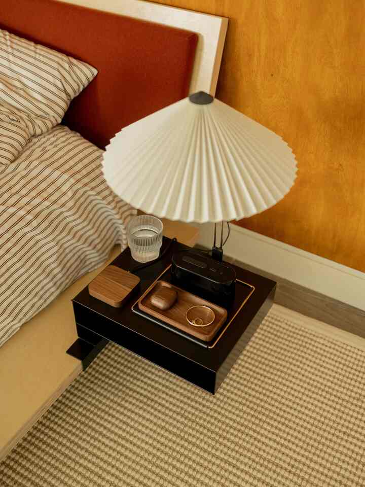 Warm brown wood-toned bedroom featuring a black nightstand with a white table lamp and wooden tray creating a cozy atmosphere