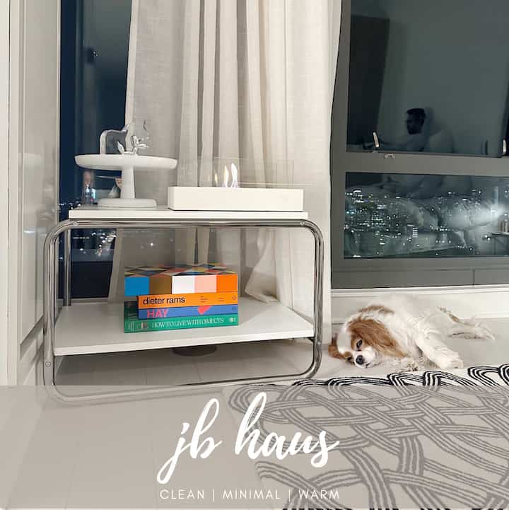 A white and natural tone living room featuring a sleek side table, linen curtains, and a relaxed dog resting on the floor