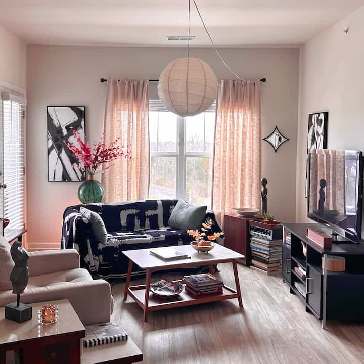 Living room with white walls and pink curtains featuring a navy sofa, coffee table, and armchair in a simple modern style