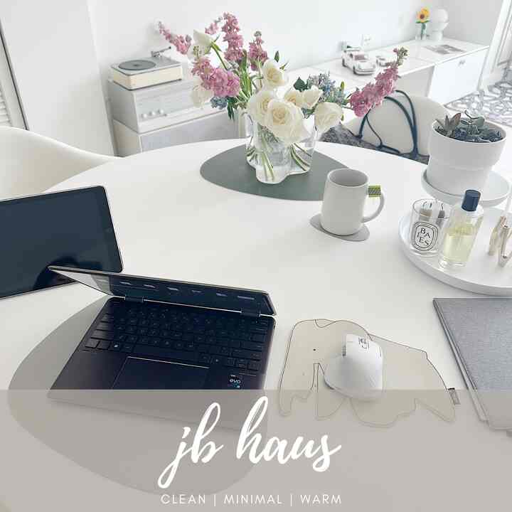 White and natural tone dining room featuring a white dining table with laptop, tablet, vase, and diffuser arranged in a simple modern remote work setting