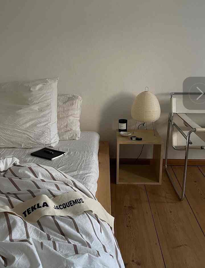 Soft natural-toned bedroom featuring wood floor and a simple side table with Akari lamp, creating a cozy atmosphere