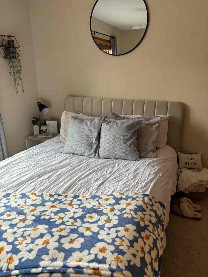 Beige-toned bedroom featuring beige walls, white bedding, round wall mirror, and cushions creating cozy ambiance