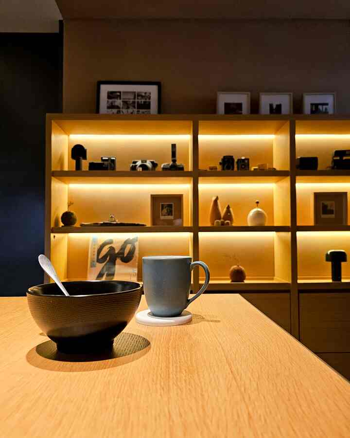 Cozy home cafe space with warm wood tone illuminated shelving and a blue mug and black bowl on a wooden dining table
