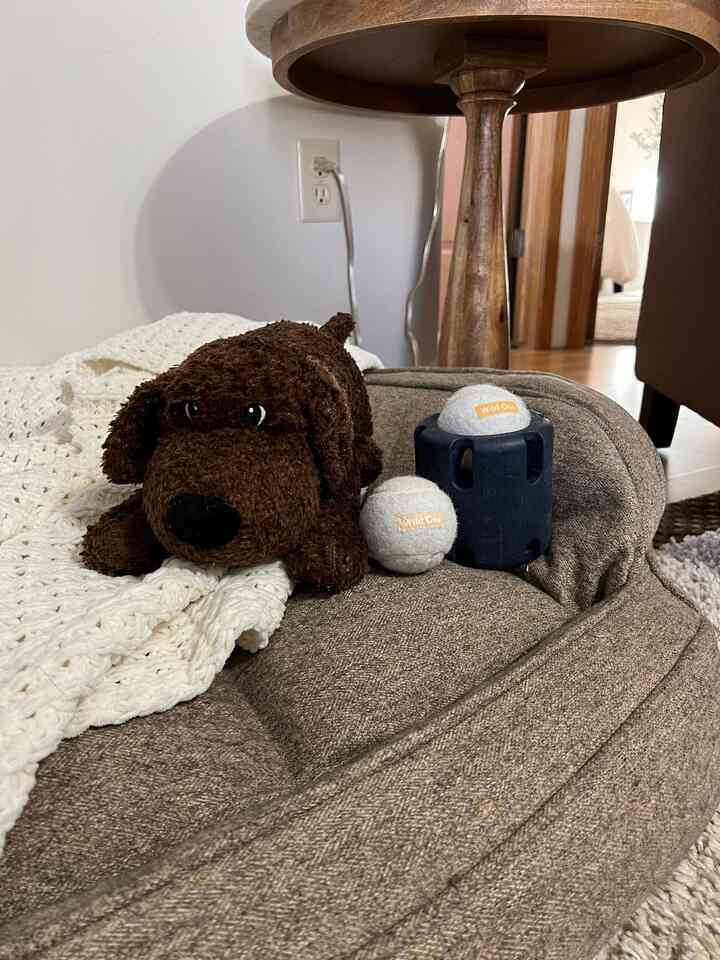 Brown-toned pet bed with white knitted blanket and dog toys arranged in a cozy pet corner
