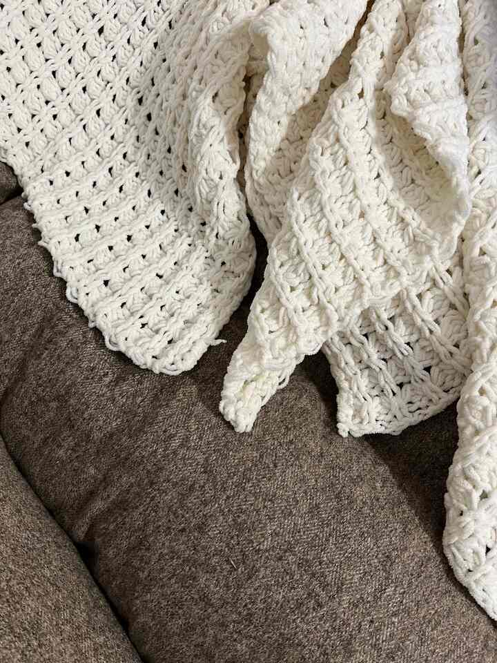 Brown sofa with a white chunky knit throw blanket draped over, creating a cozy living room atmosphere