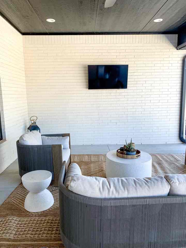 Modern outdoor living balcony with white brick wall, beige rug, sofa and round tables