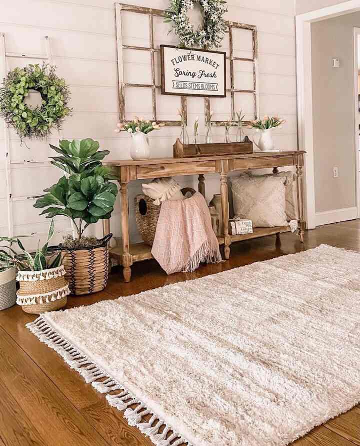 Beige and wood tone entrance space featuring wooden console, plants, and rug creating warm farmhouse style atmosphere