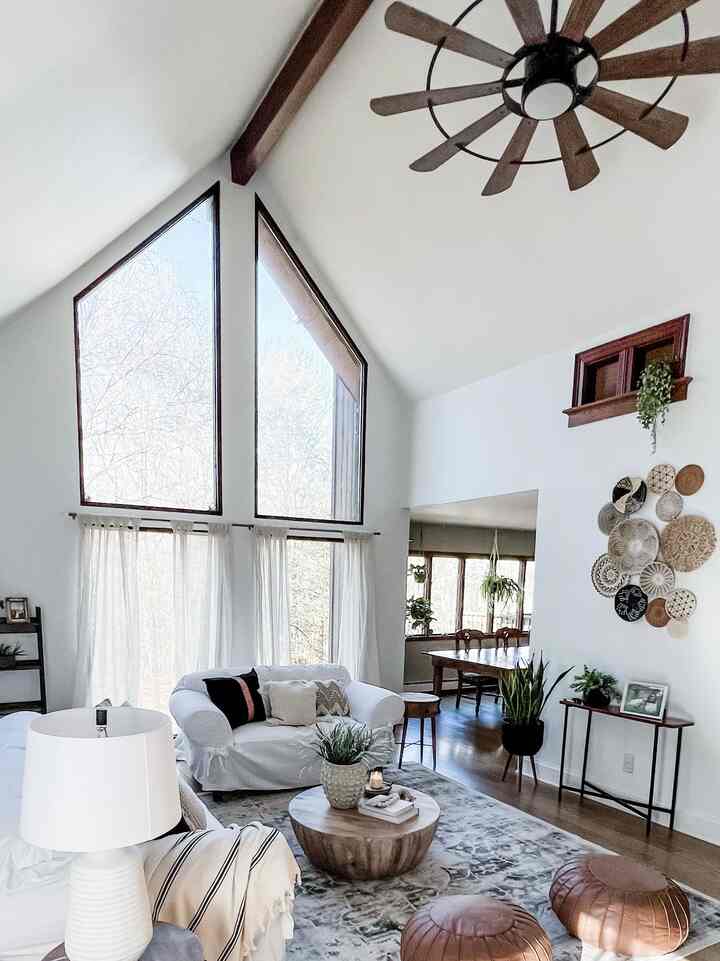 Bright white and wood-toned high ceiling living room featuring bohemian wall decor and cozy sofa in a natural style space