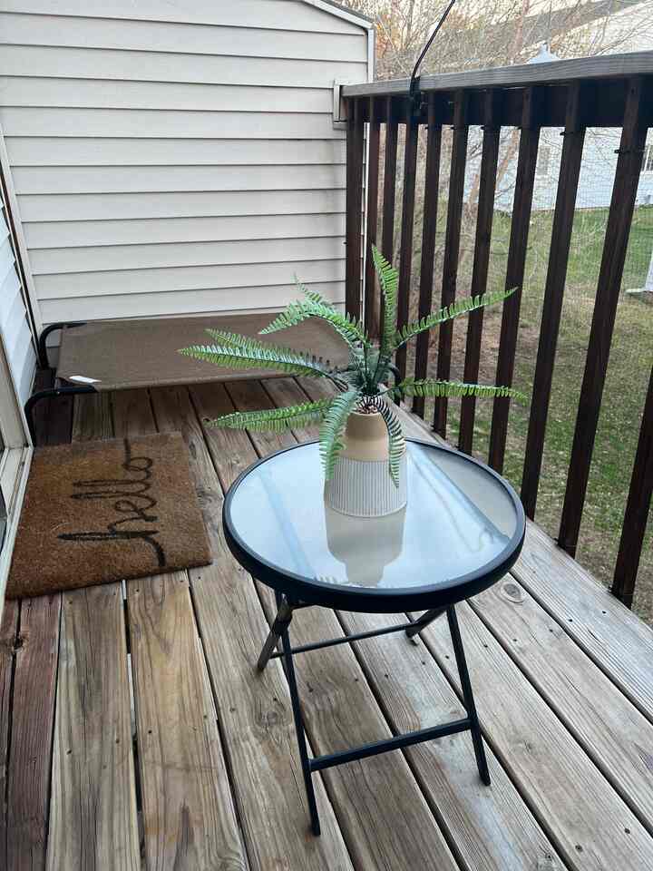 Natural wood-toned balcony featuring a transparent glass table with a decorative plant, creating a cozy outdoor atmosphere