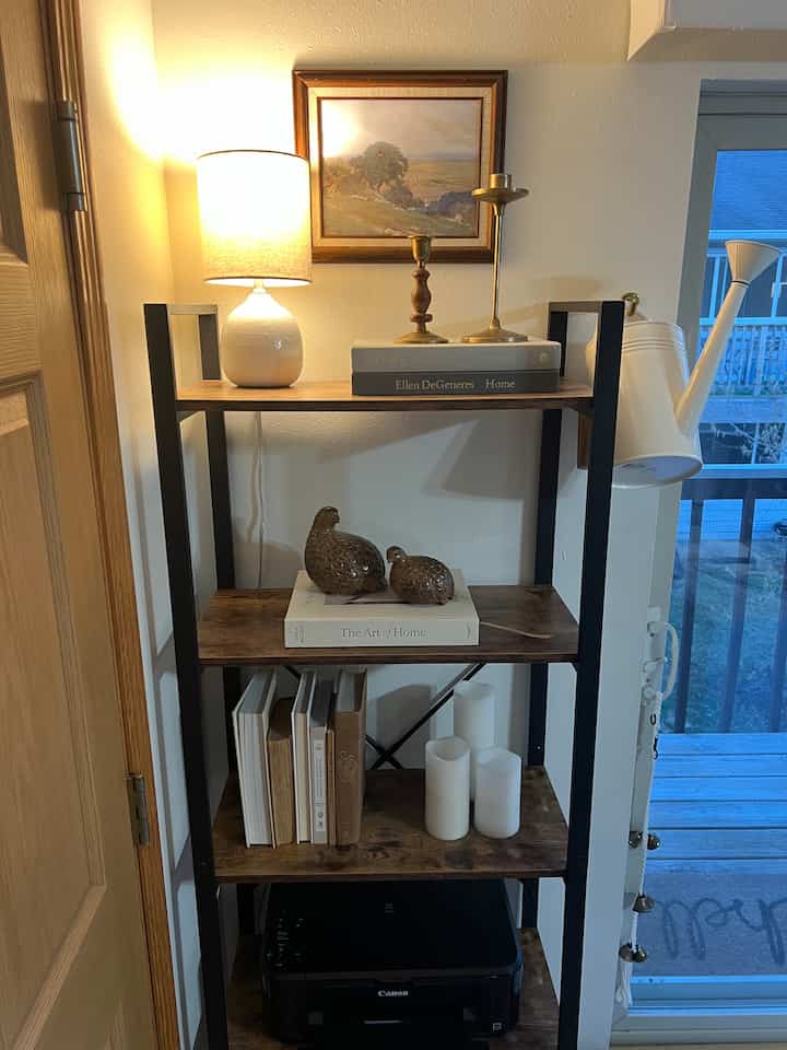 Natural brown-toned entrance featuring wooden shelves with books, ambient table lamp and decorative objets creating cozy atmosphere