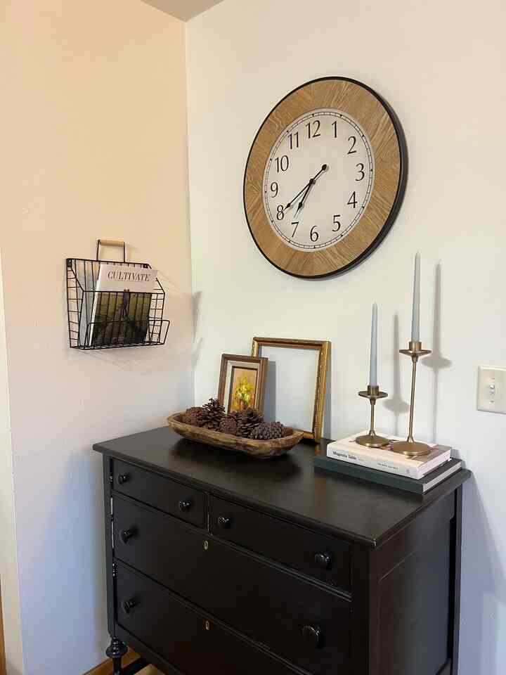 Cozy entrance with a black chest of drawers, wood-toned wall clock, and natural decor elements