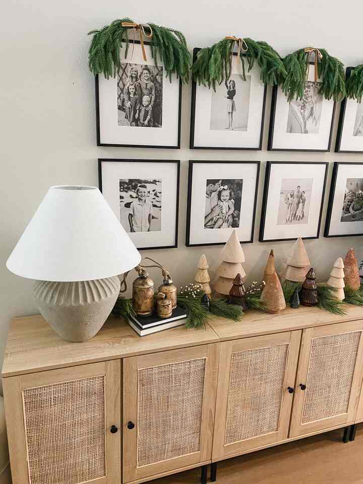 Natural color entrance space featuring rattan cabinet, table lamp, Christmas garlands, and framed gallery wall creating a cozy atmosphere
