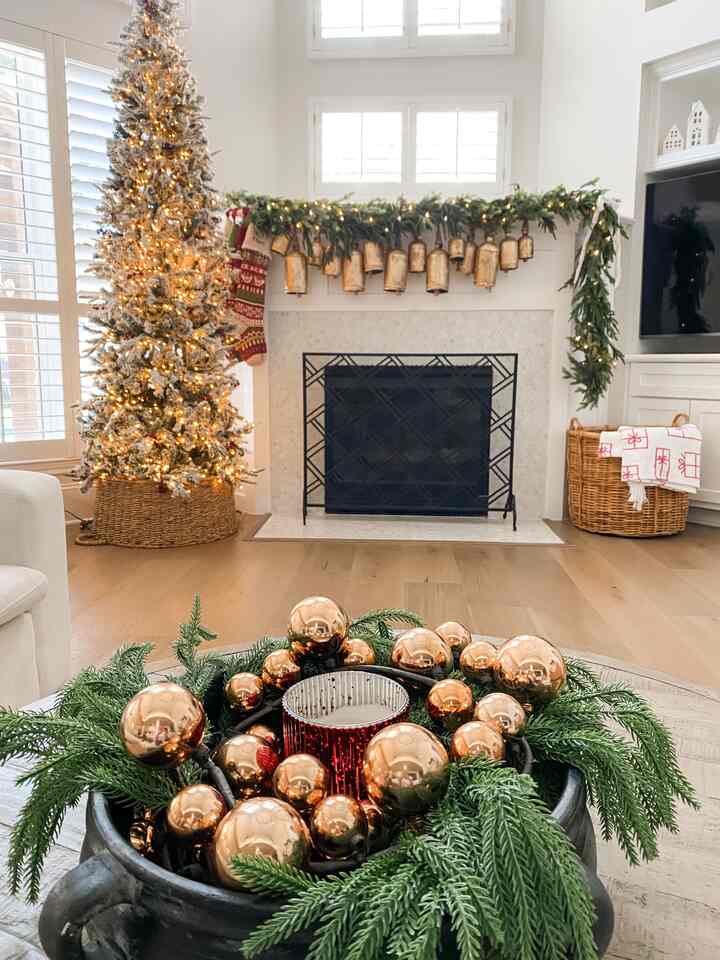 White and natural toned living room featuring a flocked Christmas tree and a gold garland-adorned fireplace with a cozy atmosphere