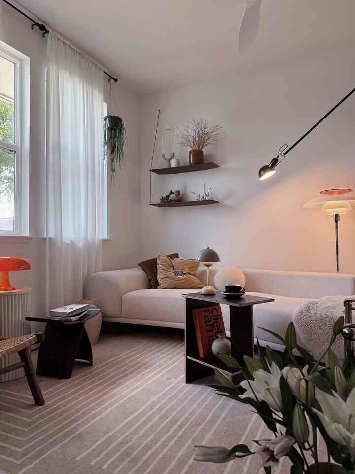 Bright white and brown toned living room featuring a Mid-Century Modern sofa, wooden shelves, rug, and lighting fixtures in harmony