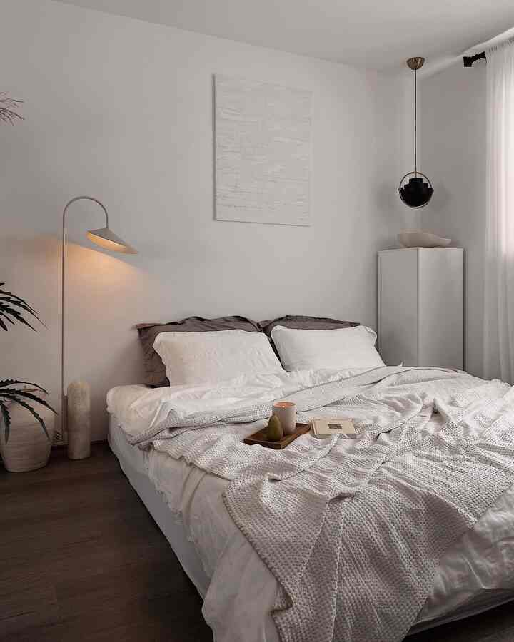 White and beige toned bedroom featuring a bed with textured blanket and floor lamp, creating a cozy natural atmosphere