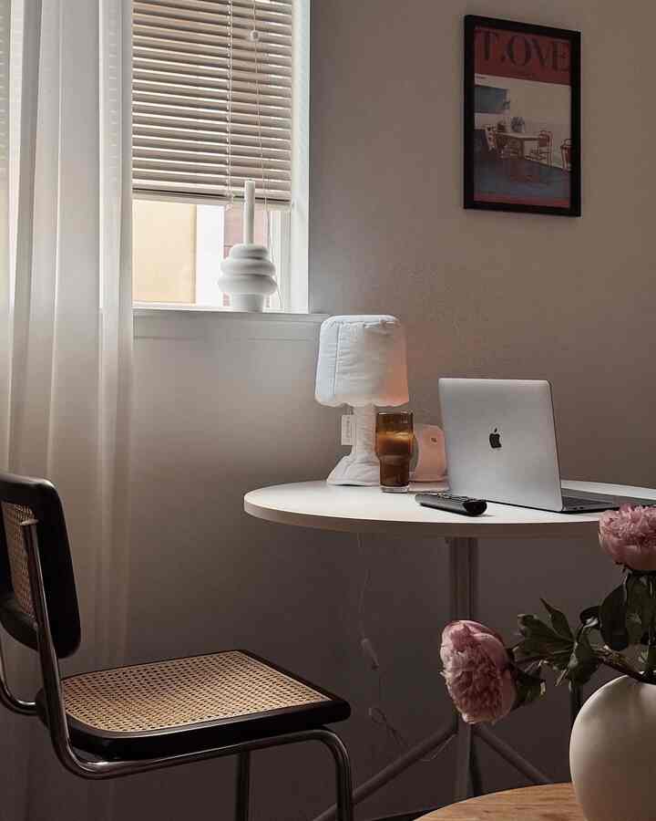 Beige and white studio living room featuring a rattan chair and round table with a Macbook and vase, creating a cozy atmosphere