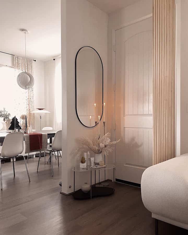 White and brown toned entrance and dining area featuring a black framed mirror and candles creating a natural and simple atmosphere
