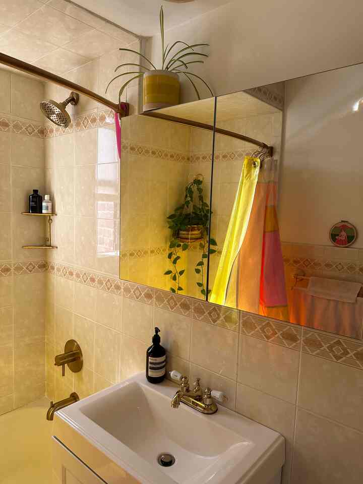 Beige tiled bathroom featuring a white sink, large mirror, and green plants creating a warm, clean atmosphere
