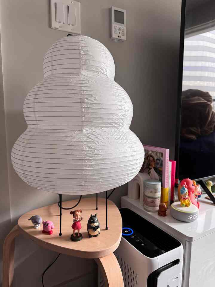 Small space with white and natural tones featuring a Japanese paper floor lamp and natural wood stool adorned with Studio Ghibli figurines, cozy atmosphere