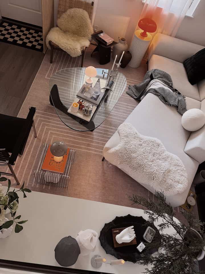 Beige and white toned living room featuring a glass coffee table, mid-century modern style sofa, and various lighting creating a warm ambiance