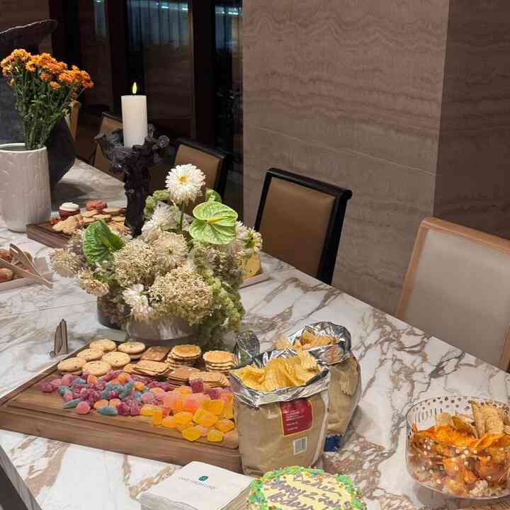 White marble dining table with brown chairs in a dining room, featuring a vase, candle, and assorted snacks creating a warm atmosphere