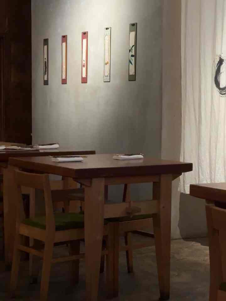 A natural wood-tone dining room in Japandi style featuring wooden tables and chairs with muted gray walls and artistic wall decor, creating a serene atmosphere