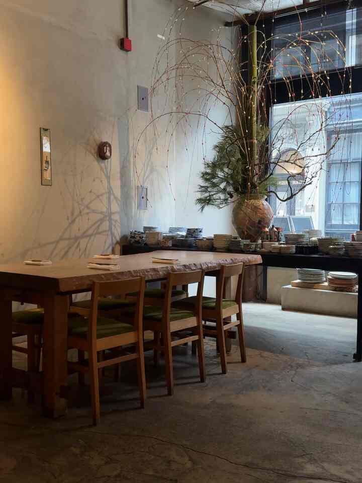 Beige and wood-toned dining room featuring a large wooden dining table with four chairs, a prominent large vase with branches, creating a natural atmosphere